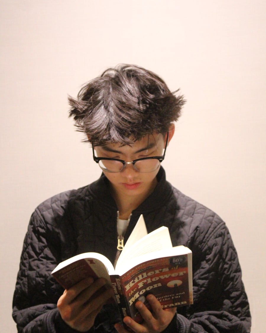 Carson reading Killers of the Flower Moon against a light wall
