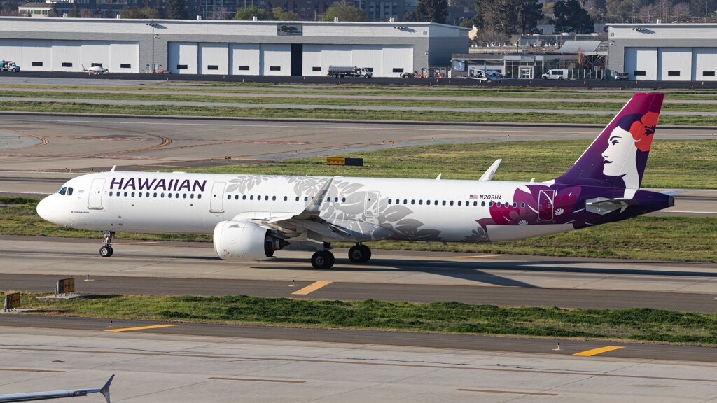 A Hawaiian Airlines aircraft taxiing across an airport runway