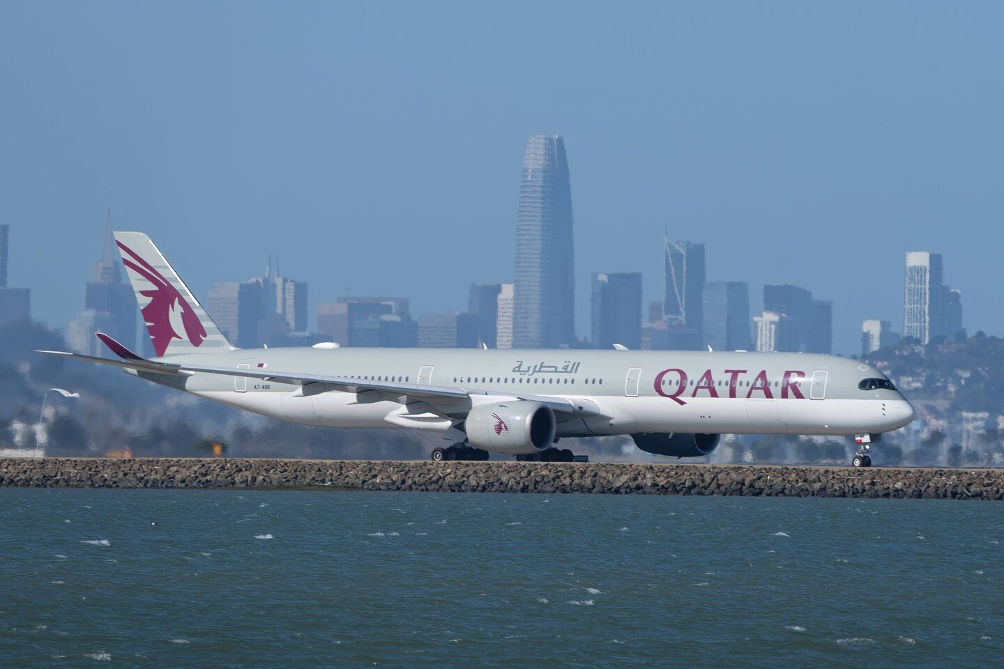 A Qatar Airways aircraft moving along the bay with the San Francisco skyline behind it