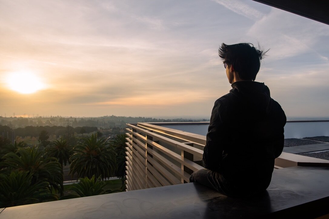 A seated person in silhouette looking toward the sun from a concrete overlook