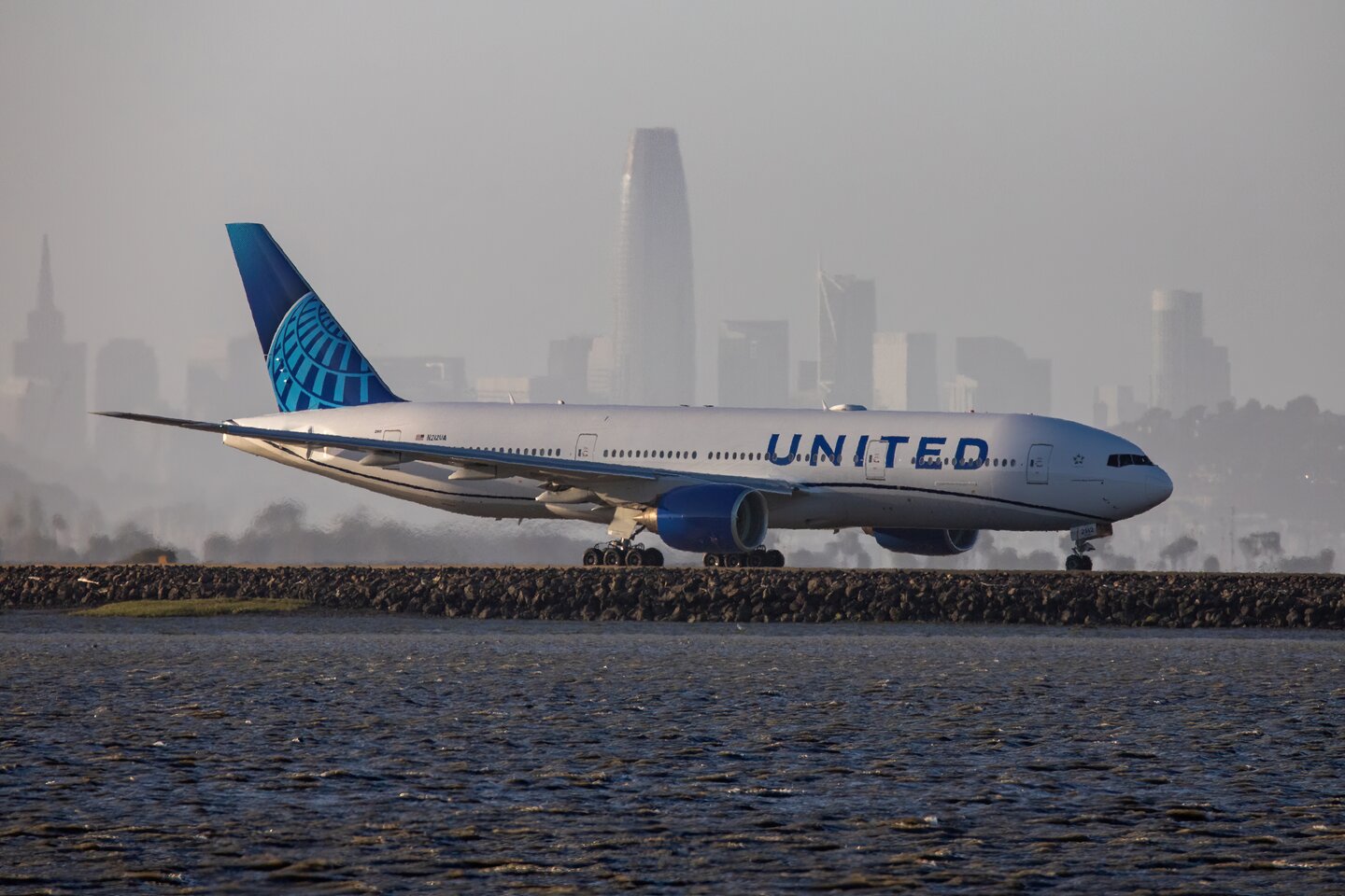 A United Airlines aircraft beside the bay with a hazy city skyline behind it